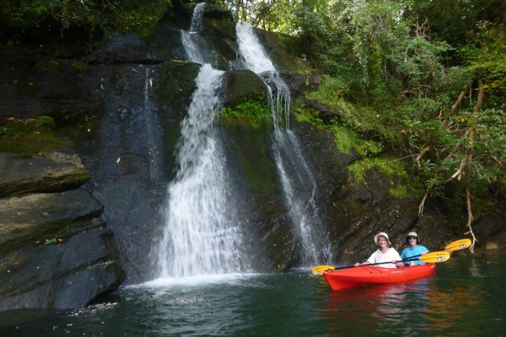 a man riding on the back of a boat next to a waterfall