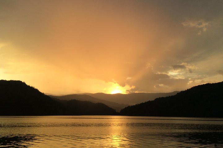 a sunset over a body of water with a mountain in the background