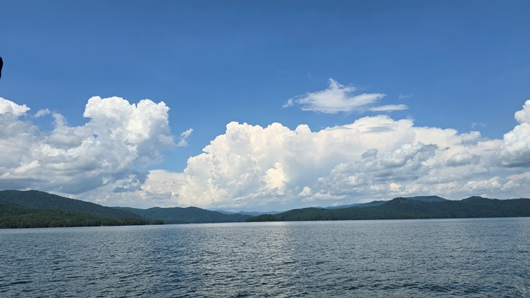 Blue sky with fluffy clouds over a lake and distant hills.