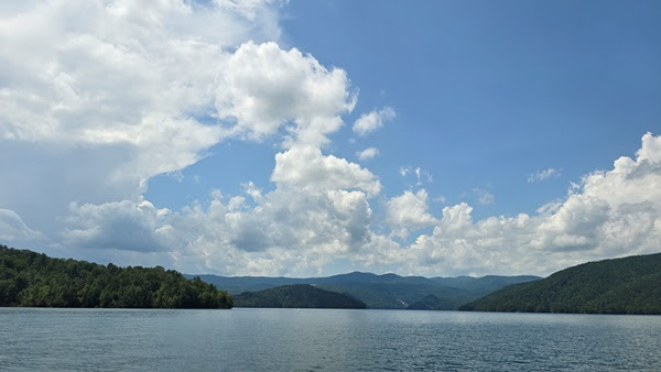 Lake with surrounding hills under a blue sky with clouds.