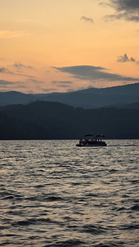 Boat on a lake during sunset with silhouetted hills in the background.