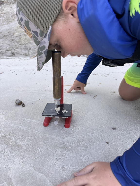 Child examining sand with homemade microscope on a beach.