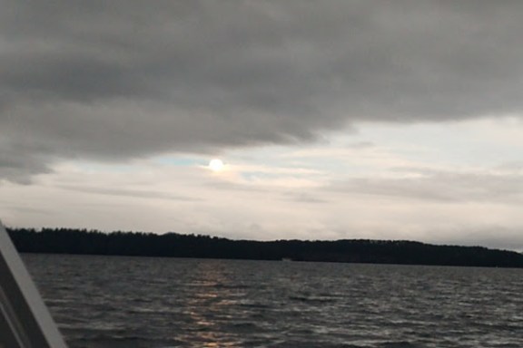 Overcast sky with a glimpse of sun over a large body of water and distant treeline.