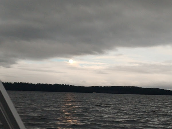 Overcast sky with a glimpse of sun over a large body of water and distant treeline.