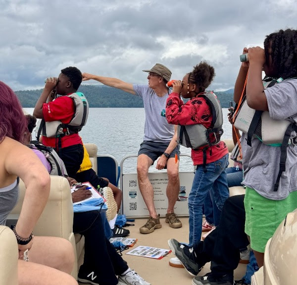 People on a boat wearing life vests, some looking through binoculars at a scenic view.