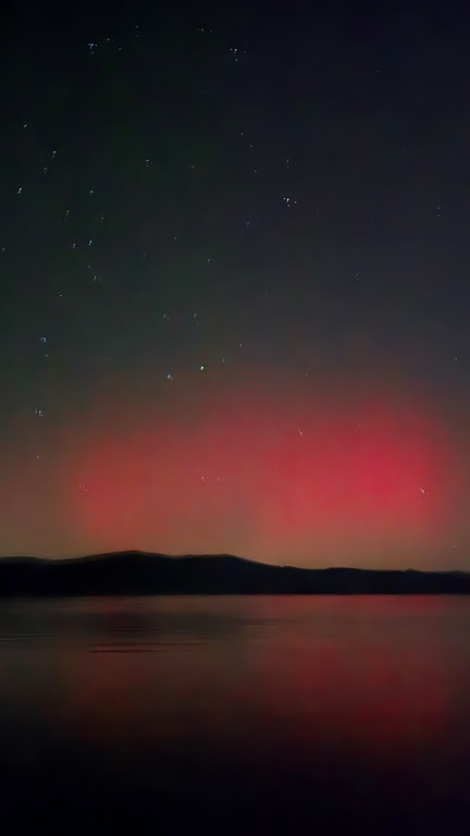 Red aurora over lake with starry night sky and dark horizon.