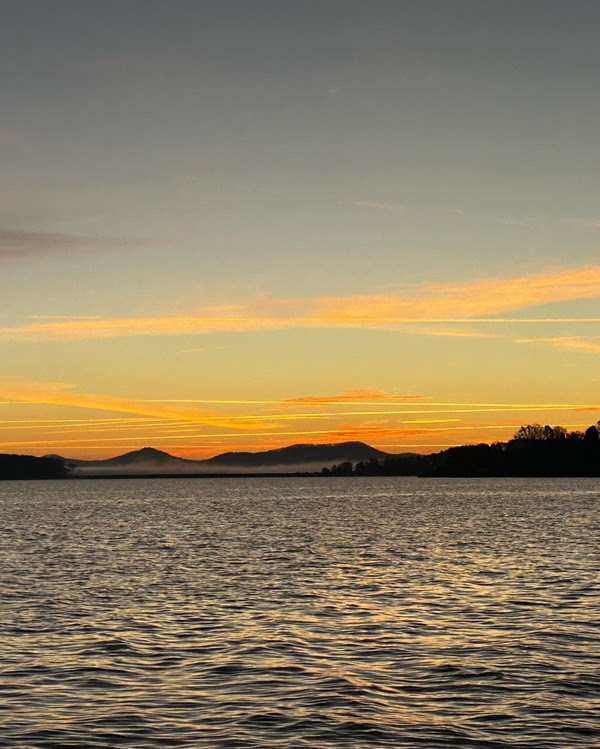 Sunset over a lake with distant hills and orange sky reflections on water.