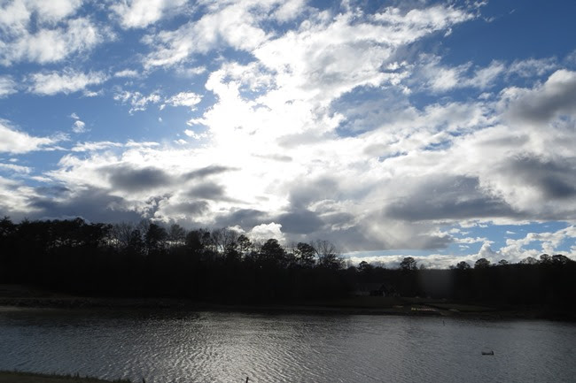 Cloudy sky over a lake with silhouetted trees on the horizon.