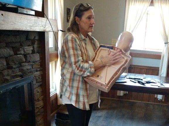 Person holding a CPR training dummy in a room with wooden walls and floor.