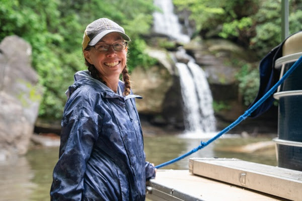 Person in raincoat smiles on a boat with a waterfall in the background.