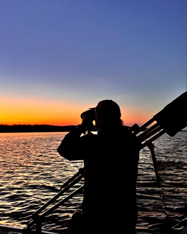 Silhouette of person with tripod by a lake at sunset.