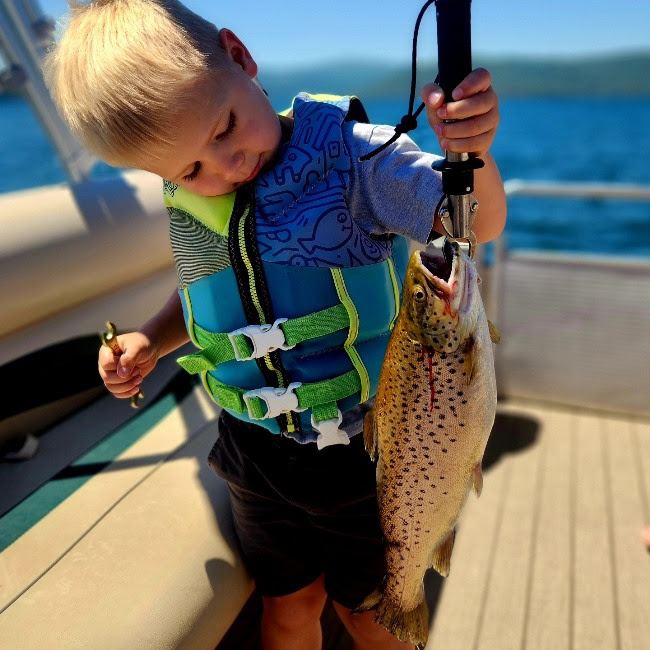 Child on a boat holding a large fish vertically, wearing a life vest.