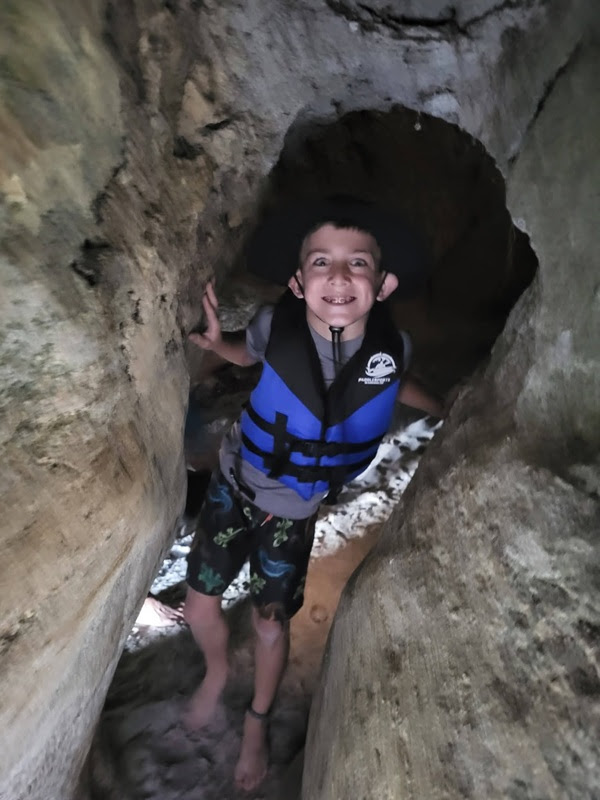 Child in blue life jacket navigating narrow rock cave.