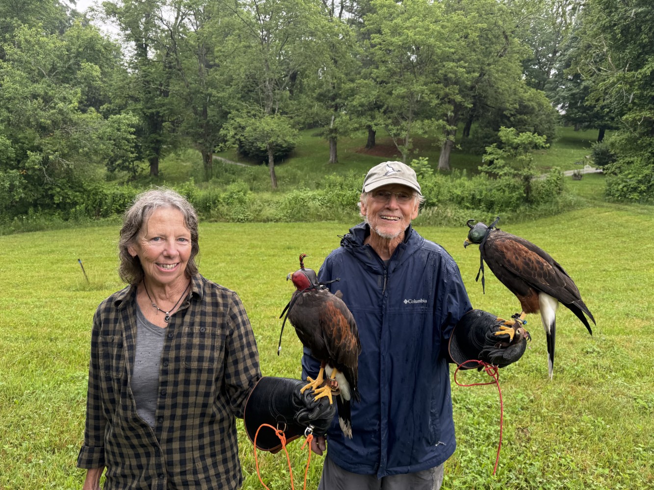 Two people smiling, each holding a falcon on their gloved hand in a grassy area.