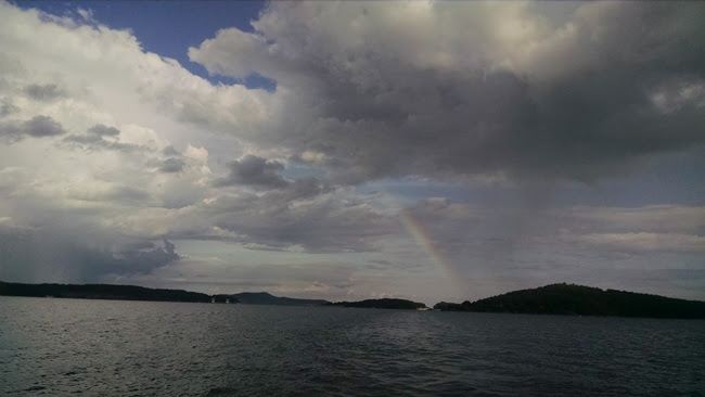 Lake with distant land, clouds, and faint rainbow.