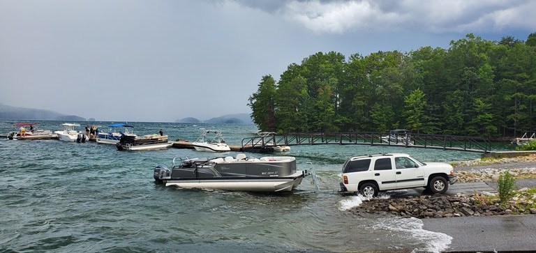 SUV launching a boat at a lakeside dock with forest in the background.