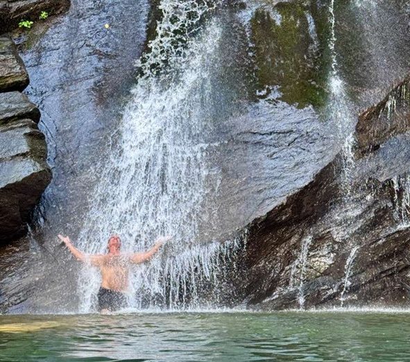 Person standing under a small waterfall on rocky terrain.