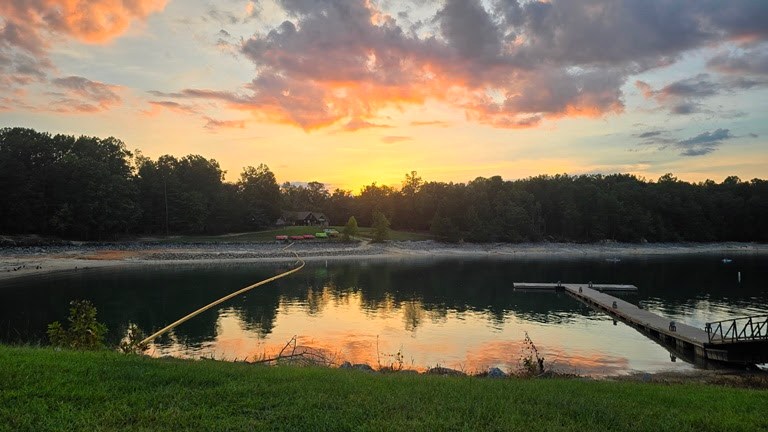 Sunset over a lake with trees and a dock.