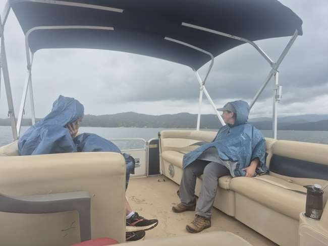 Two people in raincoats sit on a boat under a cloudy sky.