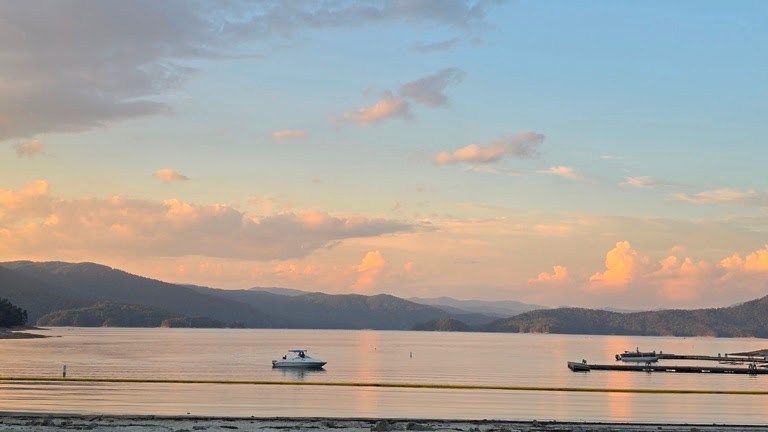 Calm lake at sunset with boats and distant mountains.