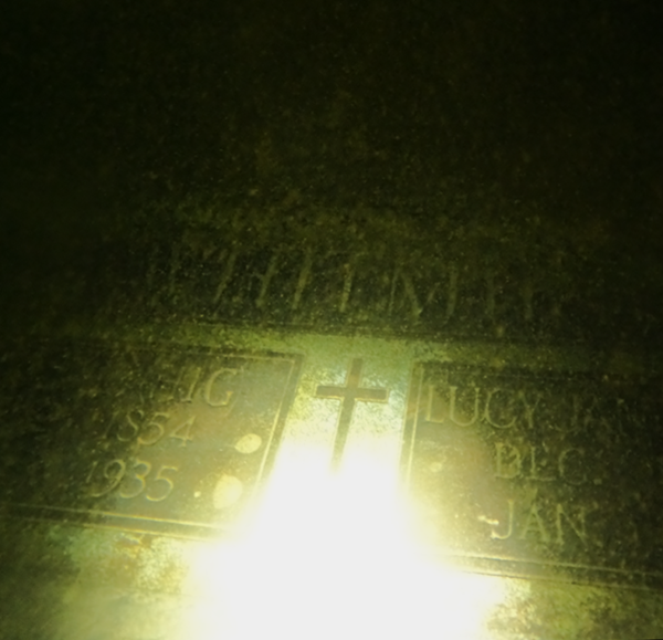 Illuminated plaque with names and dates, partially obscured by glare.